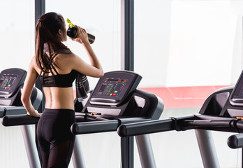 Young woman lifestyle standing drinking water on treadmill workout exercise cardio
