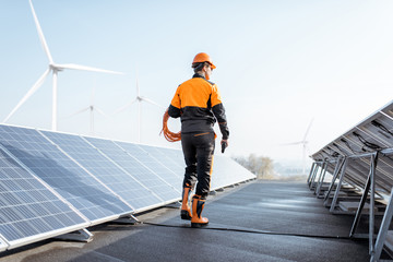 Well-equipped worker in protective orange clothing walking and examining solar panels on a...