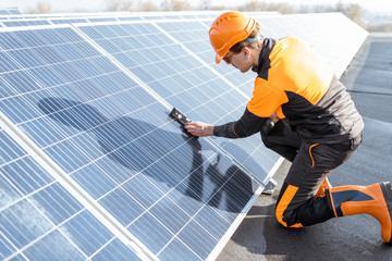 Well-equipped worker in protective orange clothing installing solar panels, measuring the angle of...