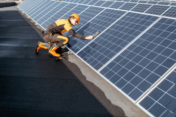 Well-equipped worker in protective orange clothing installing solar panels, measuring the angle of...