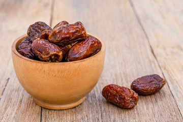 Closeup date palm fruits in wooden bowl isolated on wood table background. 
