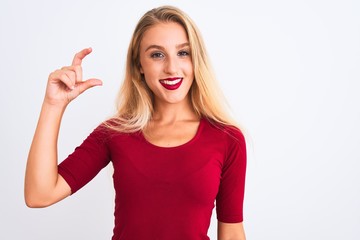 Young beautiful woman wearing red t-shirt standing over isolated white background smiling and confident gesturing with hand doing small size sign with fingers looking and the camera. Measure concept.