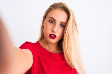 Naklejka premium Young beautiful woman wearing t-shirt make selfie by camera over isolated white background with a confident expression on smart face thinking serious
