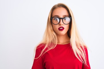 Young beautiful woman wearing red t-shirt and glasses standing over isolated white background with serious expression on face. Simple and natural looking at the camera.