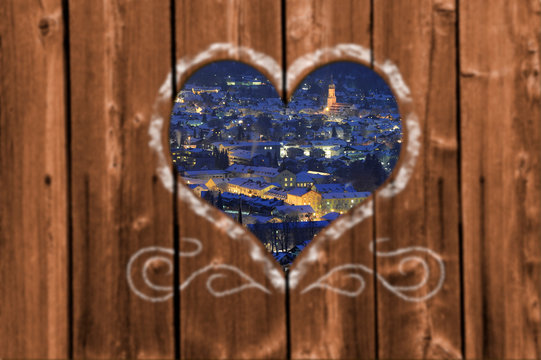Looking through a carved heart in a wooden wall to city Garmisch-Partenkirchen in Bavaria, Germany, at cold winter night