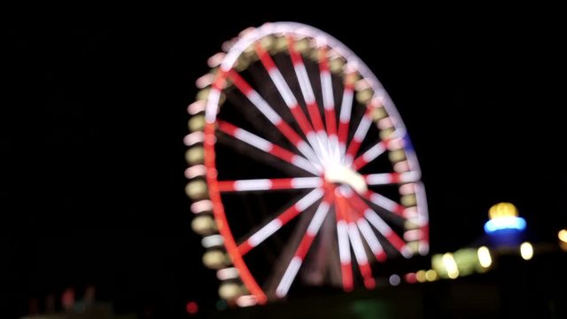 Static wide shot showing big blinking ferris wheel at night,out of focus