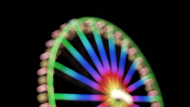 Colorful lights on giant ferris wheel,rotating slowly at night,out of focus