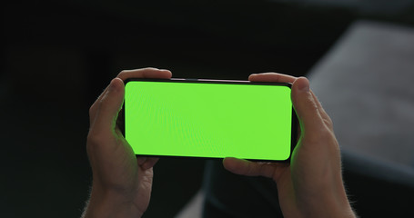 man use smartphone with green screen while lying on a couch