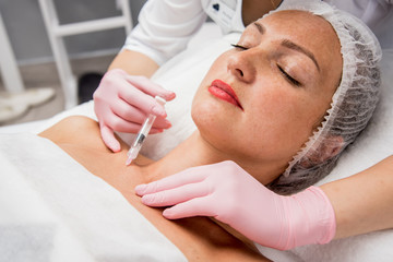 The doctor cosmetologist makes the neckline injections procedure. Young woman in a beauty salon.