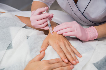 The doctor cosmetologist makes the arms injections procedure. Young woman in a beauty salon.