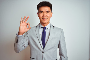 Asian chinese businessman wearing suit and tie standing over isolated yellow background smiling positive doing ok sign with hand and fingers. Successful expression.