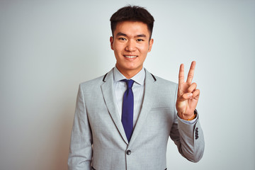 Asian chinese businessman wearing suit and tie standing over isolated yellow background showing and pointing up with fingers number two while smiling confident and happy.