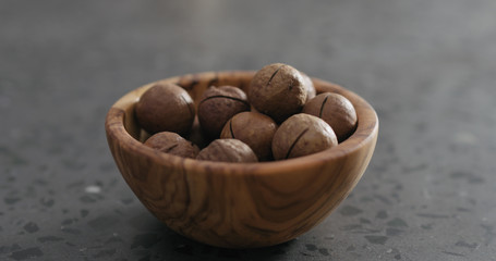 inshell macadamia nuts in olive wood bowl on terrazzo surface