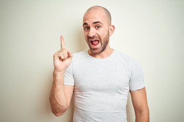 Young bald man with beard wearing casual white t-shirt over isolated background pointing finger up with successful idea. Exited and happy. Number one.