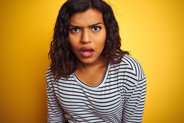 Transsexual transgender woman wearing striped t-shirt over isolated yellow background scared in...