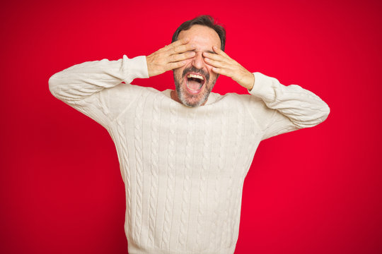Handsome middle age senior man with grey hair over isolated red background covering eyes with hands smiling cheerful and funny. Blind concept.
