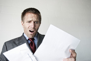 Shocked businessman opening his mail with an open mouth gasp of surprise