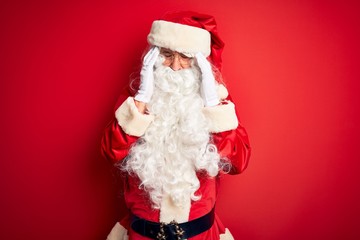 Middle age handsome man wearing Santa costume standing over isolated red background with hand on headache because stress. Suffering migraine.