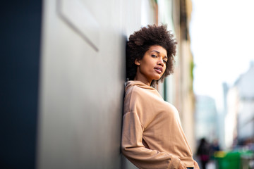 beautiful black female fashion model with afro hairstyle leaning against wall