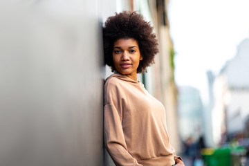 Side beautiful black female fashion model with afro hairstyle leaning against wall
