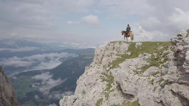 Drone flying past a rider standing on the edge of a ridge in the Dolomites.
