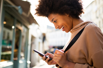 Side portrait of happy young black woman looking at mobile phone in city