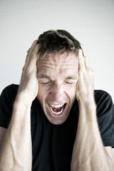 Emotional man in black T-shirt screaming with his hands on his head in frustration