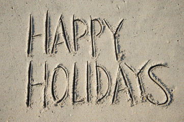 Happy Holidays message handwritten in large capital letters on smooth sand beach