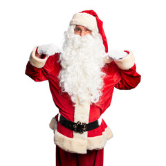 Middle age handsome man wearing Santa Claus costume and beard standing looking confident with smile on face, pointing oneself with fingers proud and happy.