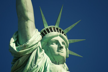 Fototapeta premium Close-up view of the weathered patina face and crown of the Statue of Liberty in bright morning sun against deep blue sky
