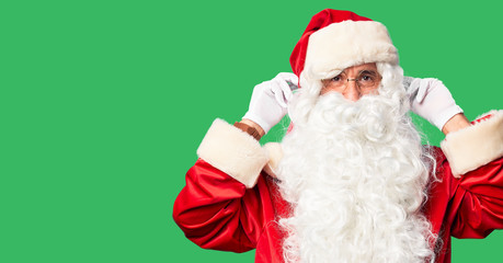 Middle age handsome man wearing Santa Claus costume and beard standing Smiling pulling ears with fingers, funny gesture. Audition problem