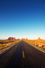 Fototapeta na wymiar Empty straight road disappearing over the horizon dotted with iconic sandstone mesas of America's wild west