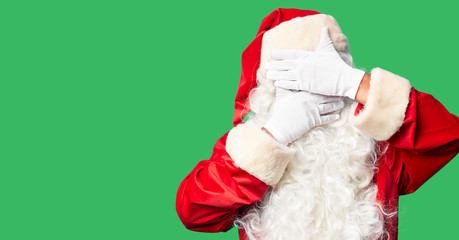 Middle age handsome man wearing Santa Claus costume and beard standing Covering eyes and mouth with hands, surprised and shocked. Hiding emotion