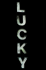 White neon "Lucky" sign glowing in white all-caps outline letters against a black background at night