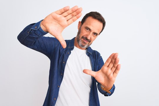 Middle age handsome man wearing blue denim shirt standing over isolated white background doing frame using hands palms and fingers, camera perspective