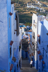 Girl travels through the narrow blue streets of the old Medina in Chefchaouen town in Morocco.	