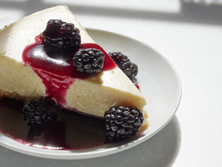 A slice of homemade cheese cake with an almond meal crust topped with blackberies with a blackberry sauce pour