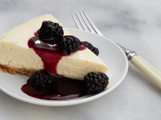 A slice of homemade cheese cake with an almond meal crust topped with blackberies with a blackberry sauce pour