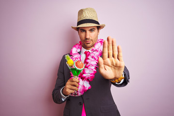 Businessman wearing suit hat hawaiian lei drinking cocktail over isolated pink background with open...