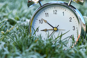 The alarm clock is in the grass covered with frost