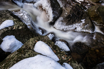 Brook of water in winter nature. Cold stream water flows between snowed stones.