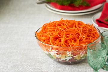 Layered vegetable salad with korean carrots in a glass bowl 