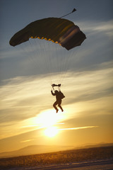 Dark silhouette of the skydiver with the canopy of the parachute during the landing against the...