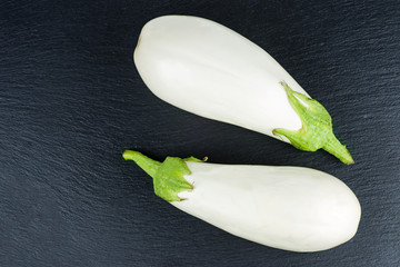 Two white eggplants on a black stone slate background
