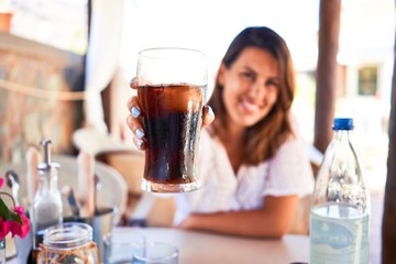 Young beautiful woman sitting at restaurant enjoying summer vacation drinking soda