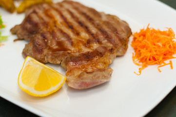 Juicy and delicious grilled meat steak with lemon, carrots, lettuce and potatoes.