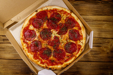 Delicious fresh pizza in cardboard box on a wooden table. Top view. Concept for home delivery of food, fast food, delivery of pizza