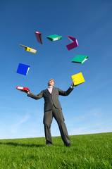 Businessman juggling file folders outdoors above a bright green meadow