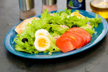 Salad with tuna, eggs, tomato, olives, spices and croutons, sauce or oil on blue plate
