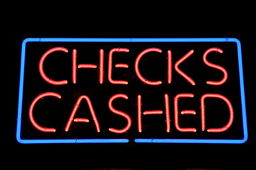 Night view of bright red Checks Cashed neon sign with blue outline hanging outdoors in a window